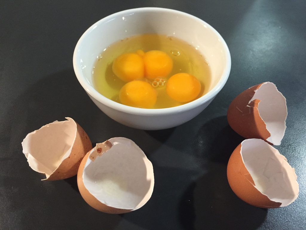 egg shells next to bowl with egg yolks and whites