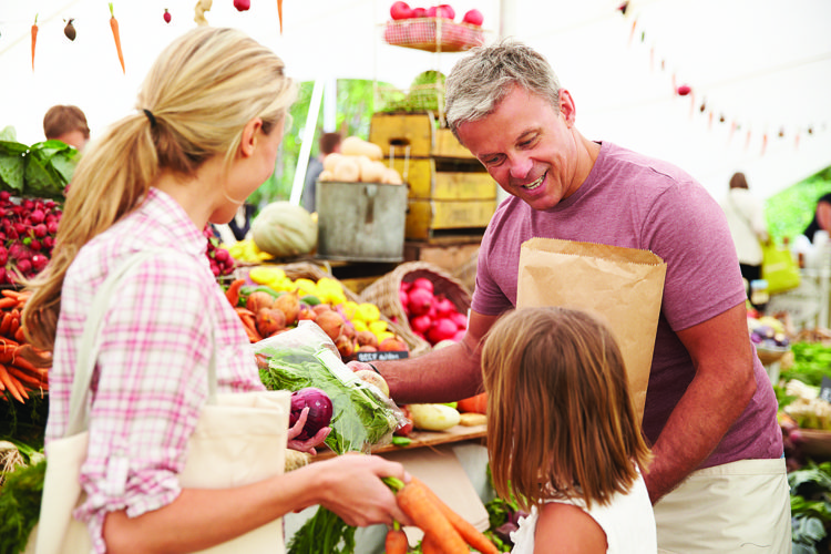 Family Buying Fresh Vegetables At Farmers Market Stall